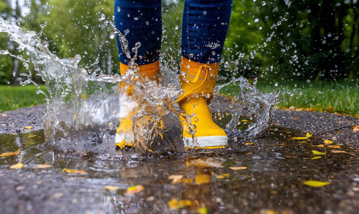 A child in yellow rain boots jumps in a puddle